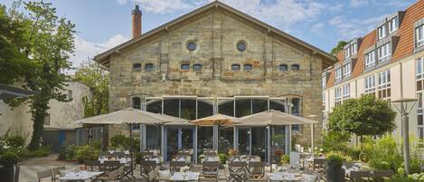 A stone building with a large patio area featuring outdoor seating and umbrellas.