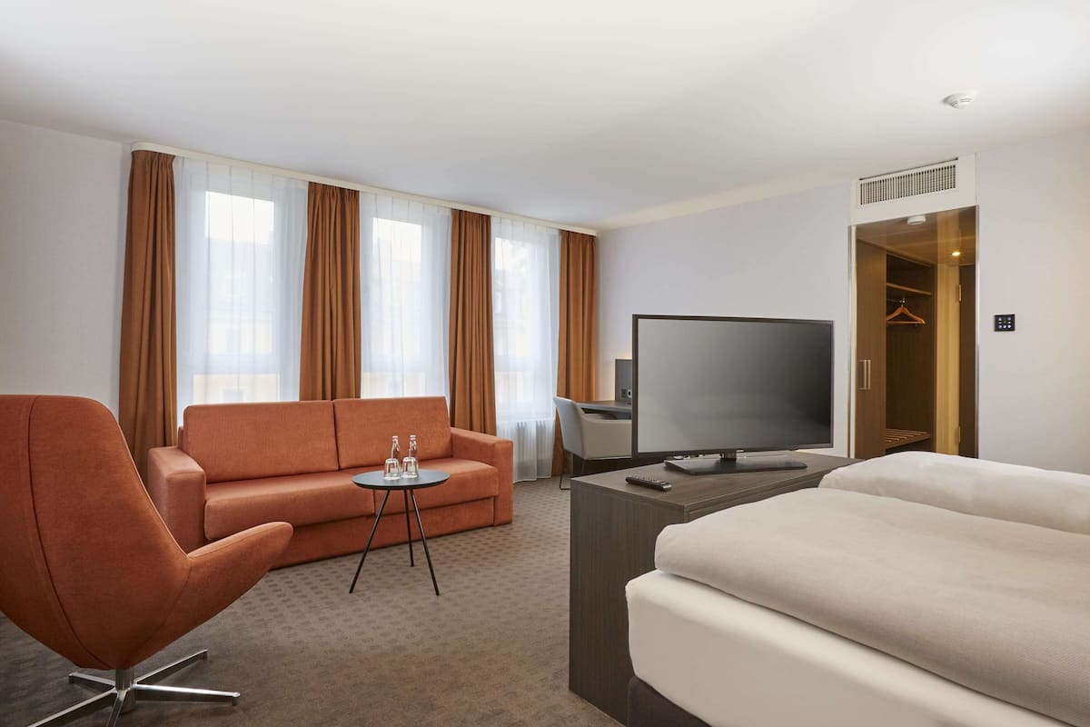 Une chambre d’hôtel comprenant un canapé, un bureau avec un téléviseur à écran plat, un lit et un dressing.