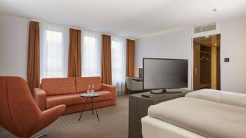 A hotel room with a sofa, a desk with a flat-screen TV, a bed, and a walk-in closet.
