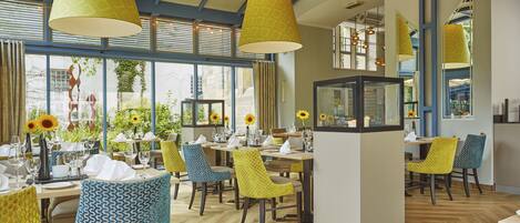 Un restaurante con una decoración moderna, que presenta sillas con estampado amarillo, mesas de madera e iluminación colgante amarilla de gran tamaño.