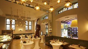 A dining area with round tables, chandeliers, and large windows.