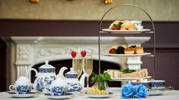 A tea service set with a three-tiered dessert stand, a fireplace, and decorative blue roses. - The Victoria Hotel Manchester by Compass Hospitality (Oldham)