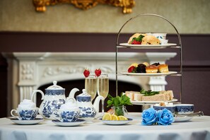 Un service à thé comprenant un présentoir à gâteaux à trois niveaux, une cheminée et des roses bleues décoratives.