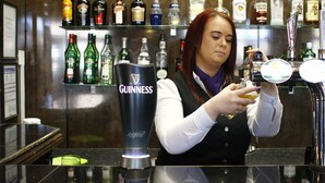 A bartender preparing a drink behind a bar with various liquor bottles and a Guinness tap. - The Victoria Hotel Manchester by Compass Hospitality (Oldham)