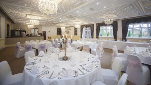 A banquet hall with round tables set for a formal event, chandeliers, and large windows with curtains. - The Victoria Hotel Manchester by Compass Hospitality (Oldham)