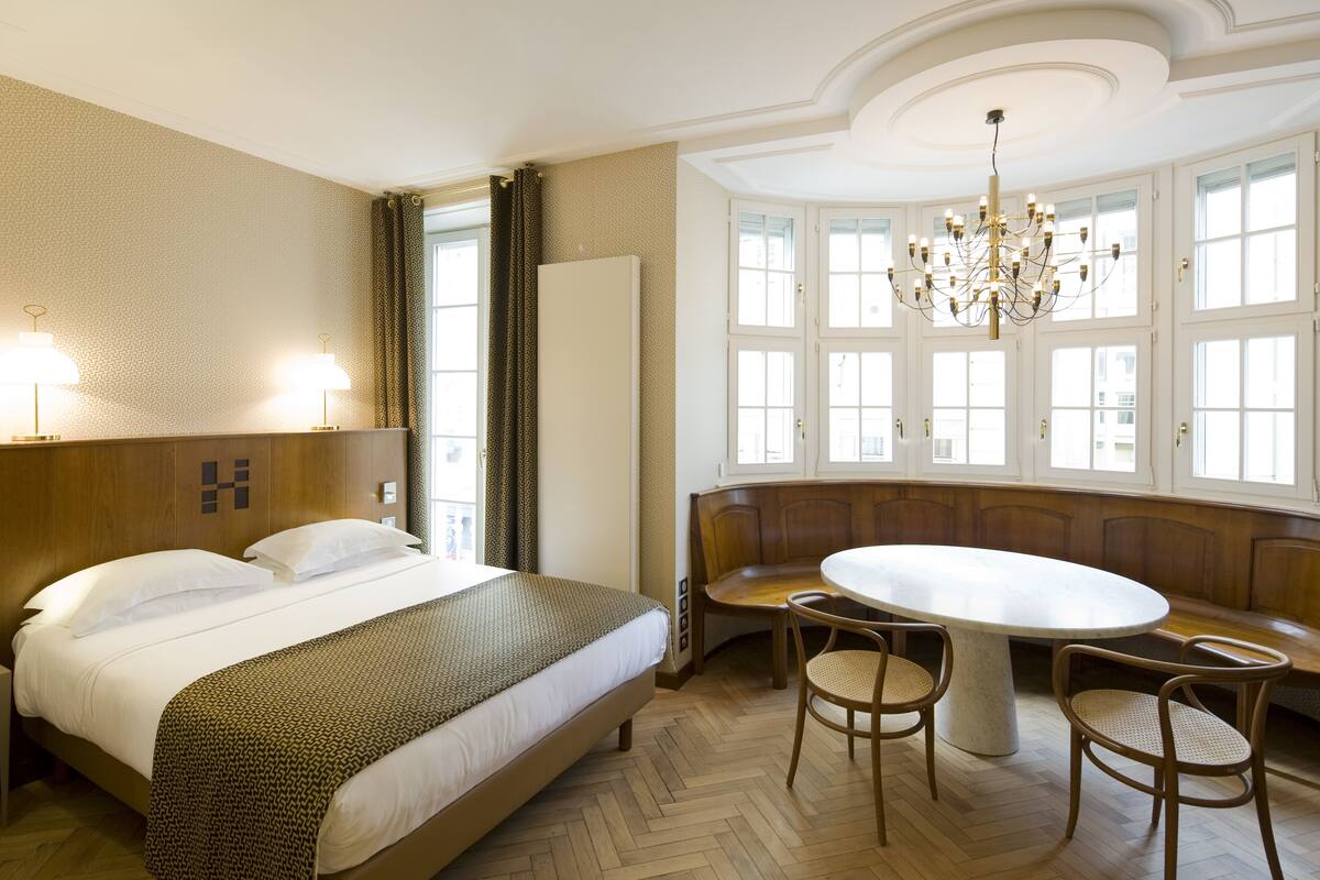 A hotel room with a large bed, a round dining table, and a bench.