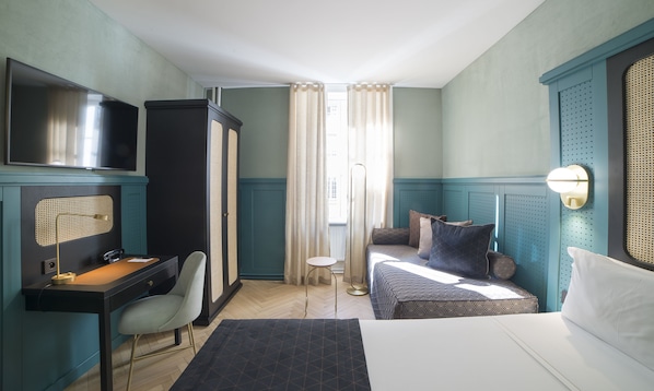 Habitación de hotel con cama, escritorio, silla, televisor y ventana con cortinas.