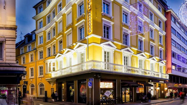 A multi-story hotel with a yellow facade, multiple balconies, and a ground-level entrance with shops. - Hotel Hannong (Strasbourg)