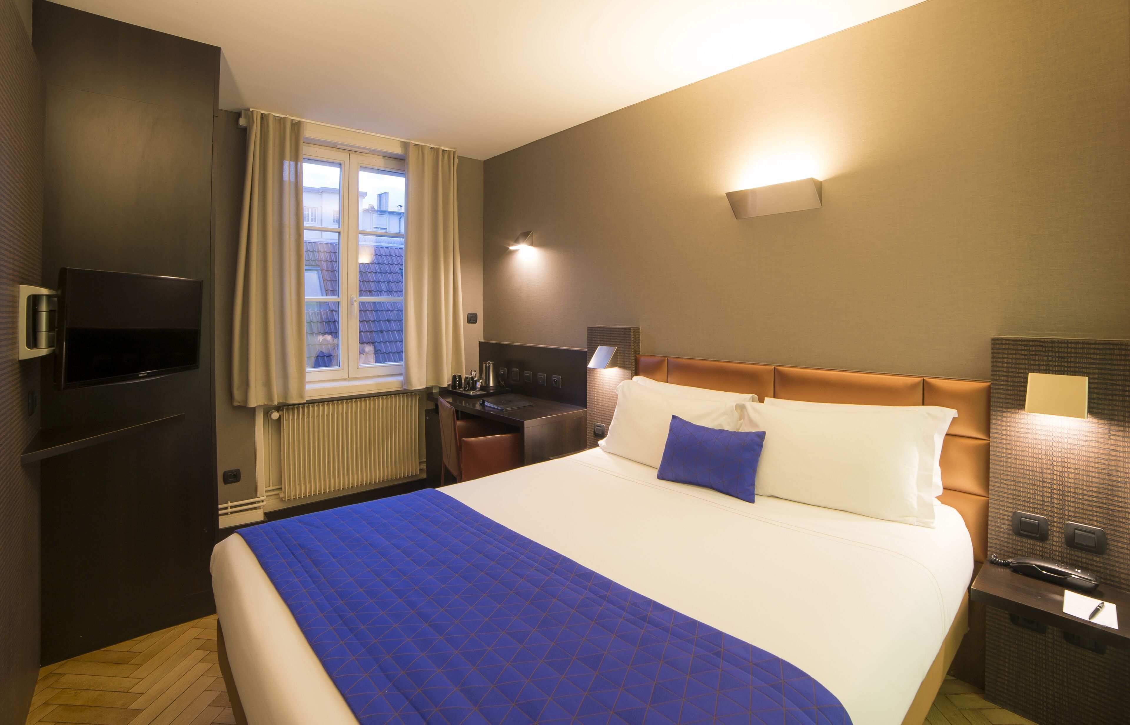 Una habitación de hotel con una cama grande, un escritorio, un televisor y una ventana con cortinas.