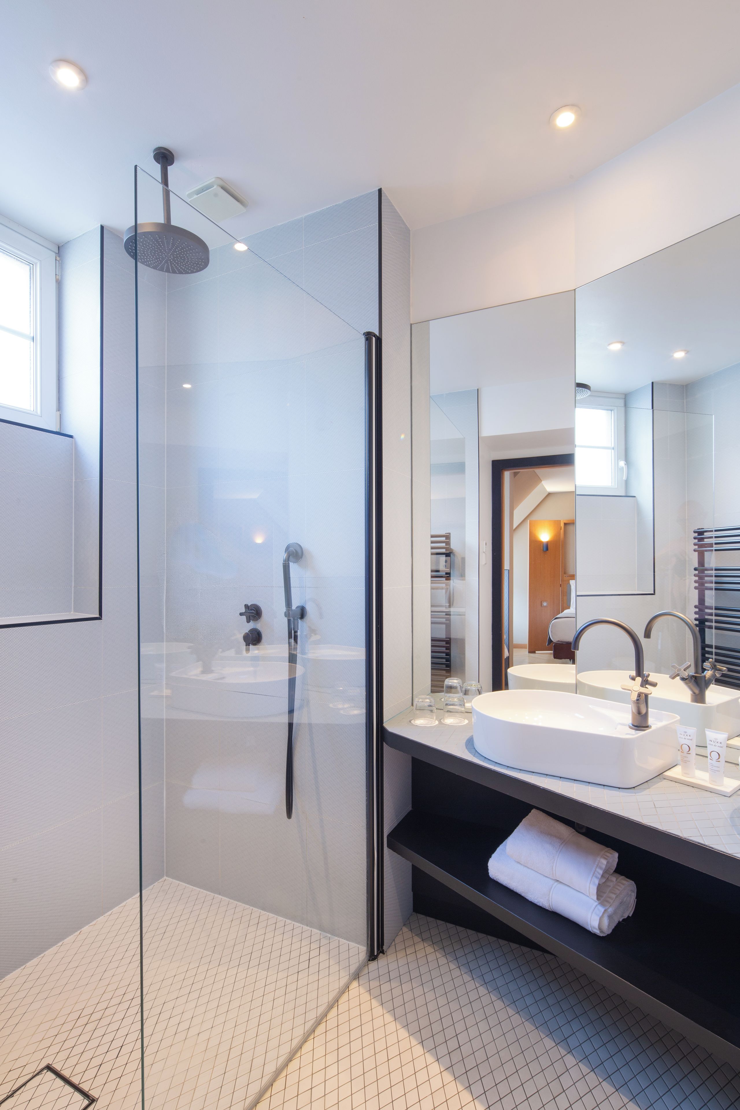 A modern bathroom with a glass-enclosed shower, a large mirror, and a white sink.