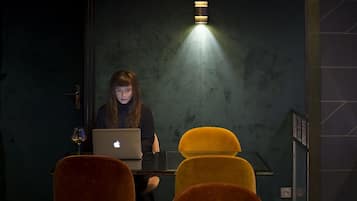 A person working on a laptop in a dimly lit room with a single light source above.