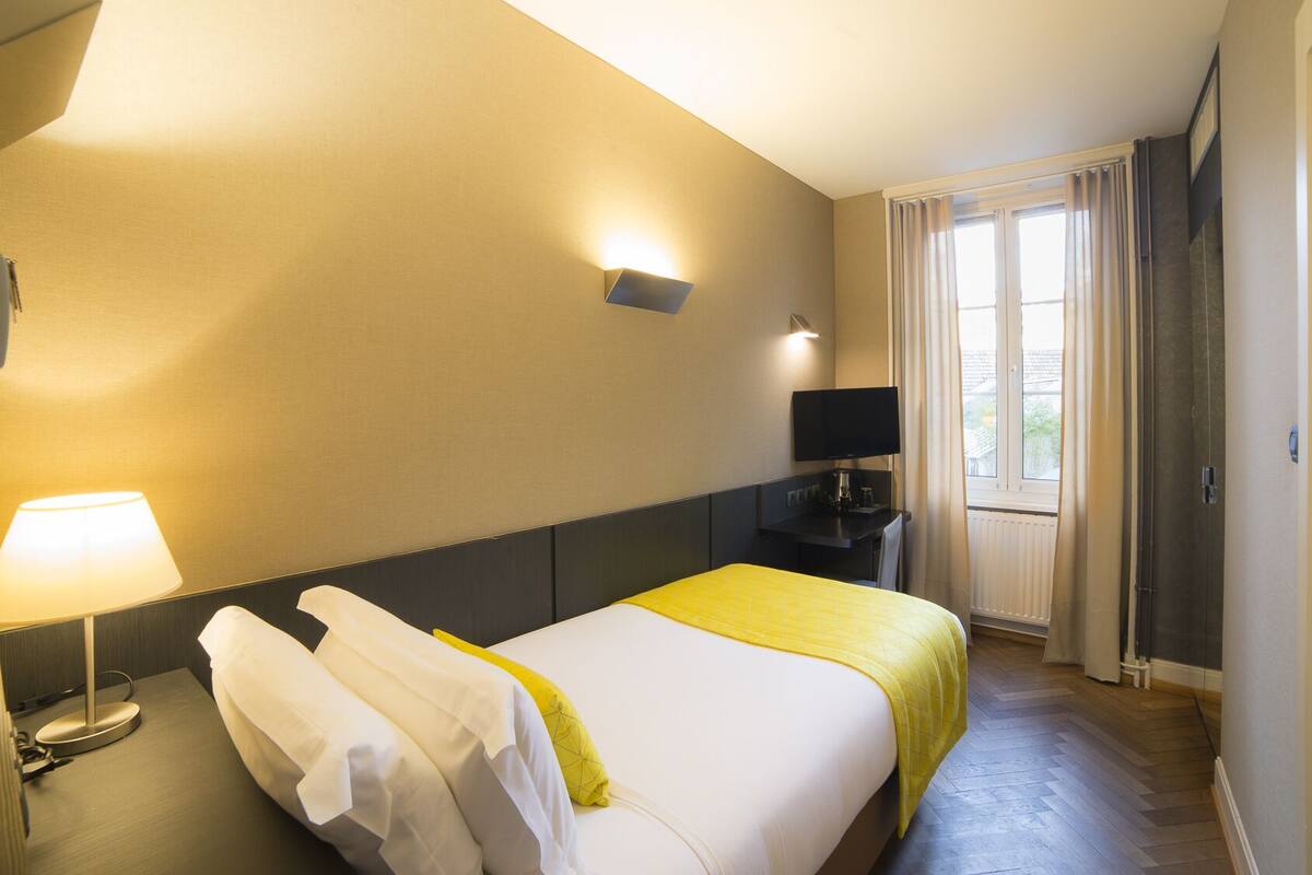 A hotel room with a bed, a desk, a flat-screen TV, a lamp, and a window with curtains.