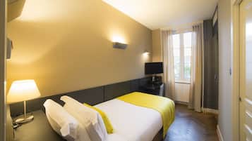 Quarto de hotel com cama, escrivaninha, televisão de tela plana, luminária e janela com cortinas.