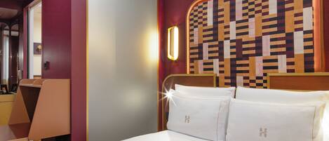 Una habitación de hotel con una cama grande, un cabecero de diseño geométrico, una mesita de noche con lámpara y un espejo en la pared.