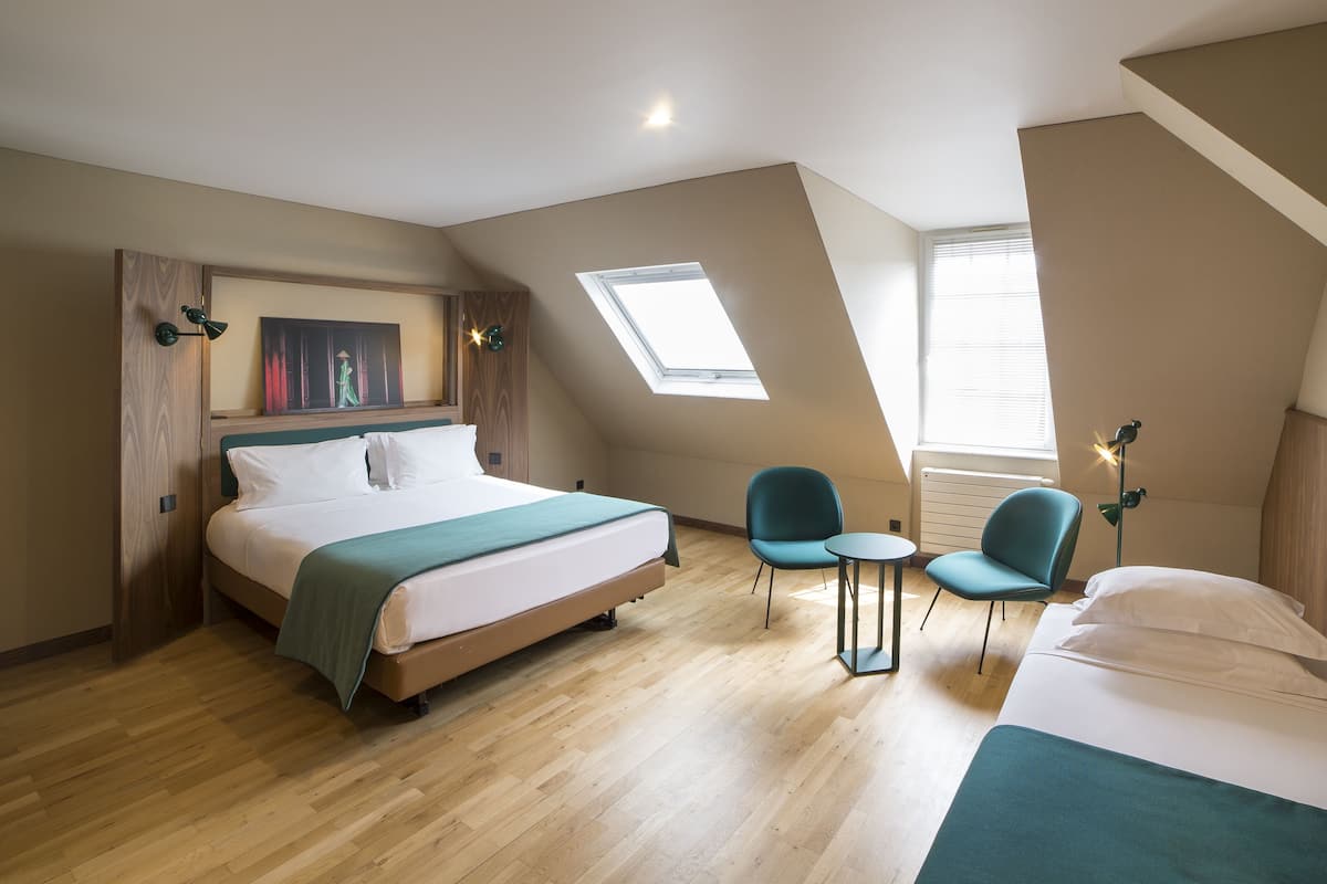 A bedroom with a large bed, a small table, two chairs, a skylight, and a TV mounted on the wall.