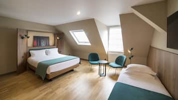 A bedroom with a large bed, a small table, two chairs, a skylight, and a TV mounted on the wall.