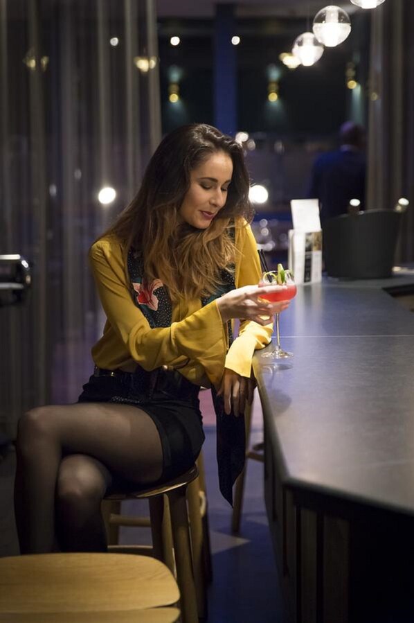 A person seated at a bar in a dimly lit indoor setting with vertical light fixtures.
