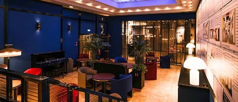 A lobby with a piano, seating areas, a staircase, and a glass ceiling.