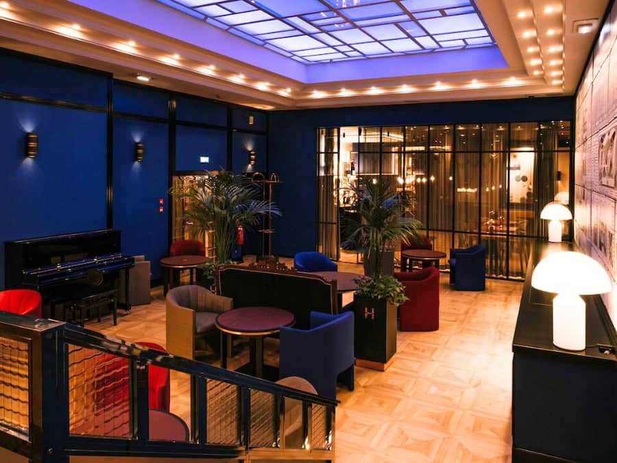 A lobby with a piano, seating areas, a staircase, and a glass ceiling.