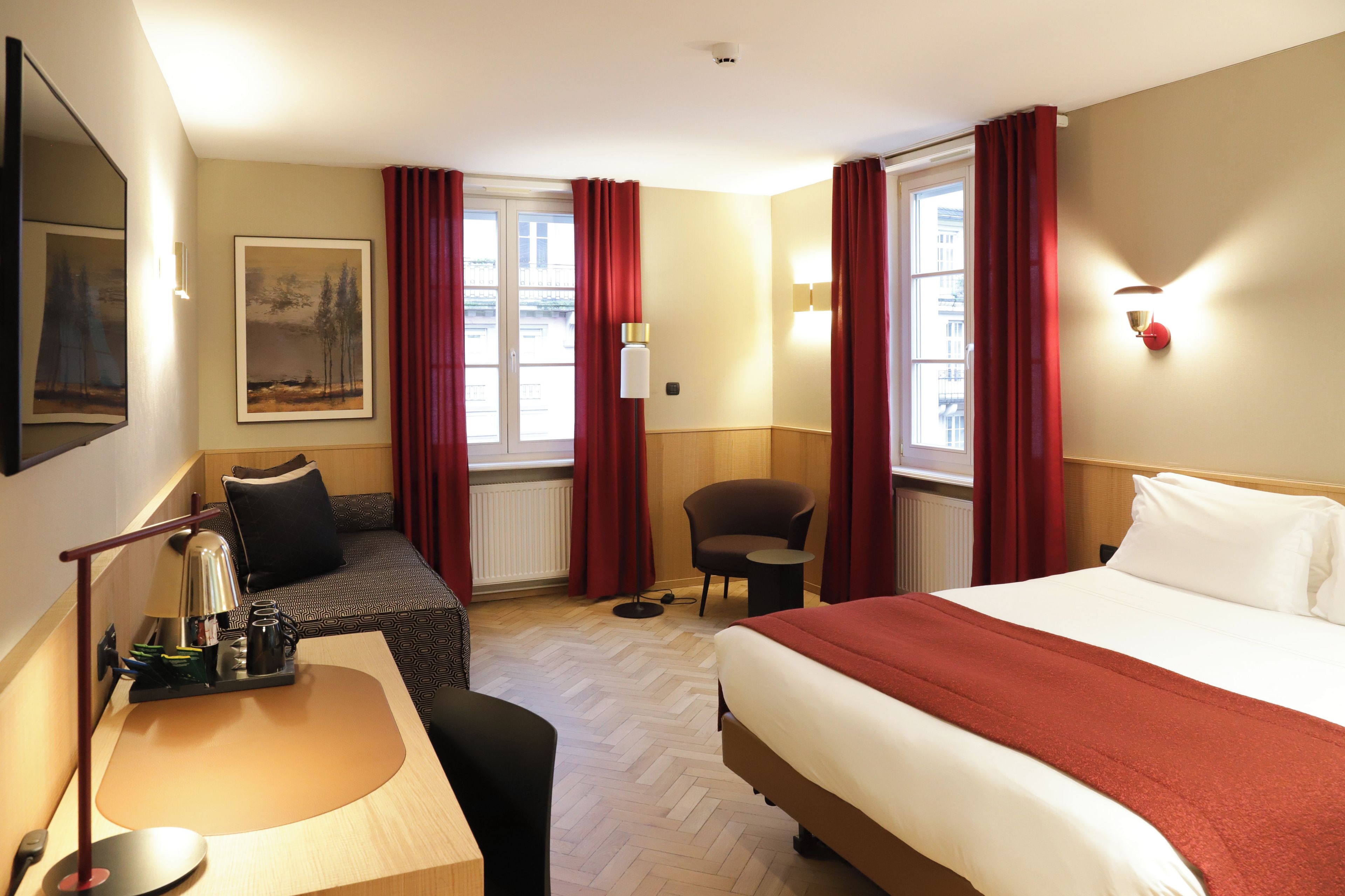 A hotel room with a bed, a desk, a chair, and a window with curtains.