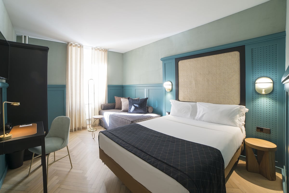 A hotel room with a large bed, a desk, a chair, and a TV.
