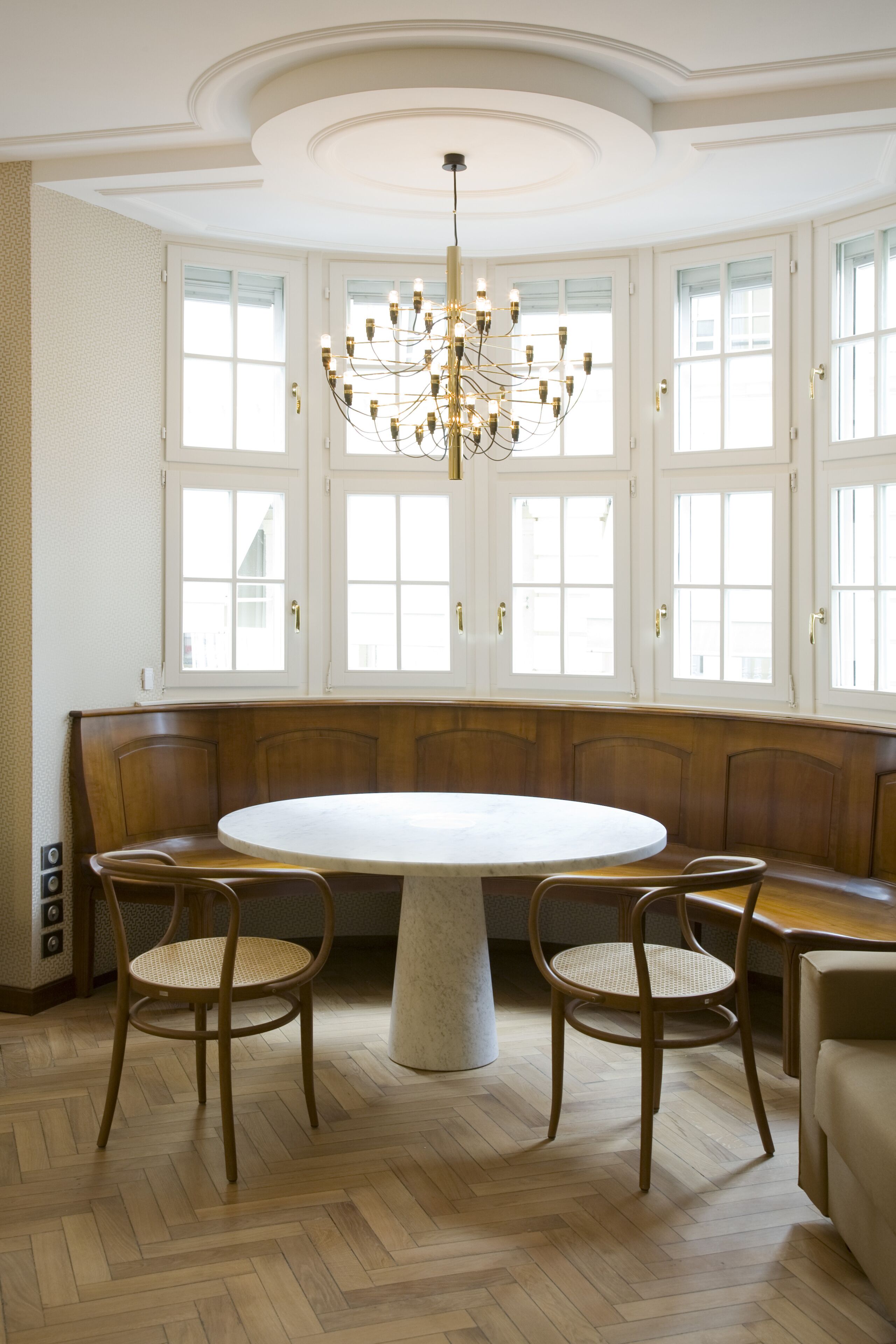 A dining area with a round table, wooden bench seating, and a chandelier.