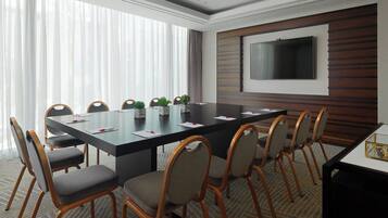 Une salle de conférence équipée d’une grande table, de chaises, d’un téléviseur fixé au mur et d’une fenêtre avec des rideaux.