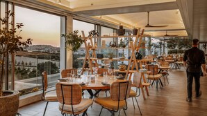 Un comedor moderno con ventanas amplias, mobiliario de mimbre y vistas a la ciudad.