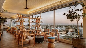 Amplia sala de estar con muebles de madera, una estantería escalonada y grandes ventanales con vistas a la ciudad.
