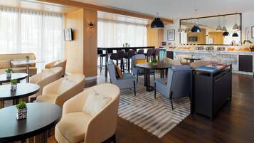 A modern living room with a sofa, armchairs, a dining table, and a kitchen area with a marble countertop and hanging pendant lights.