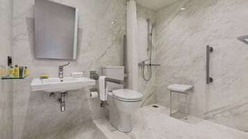 Un baño moderno con suelo de mármol, lavabo blanco, inodoro y zona de ducha.