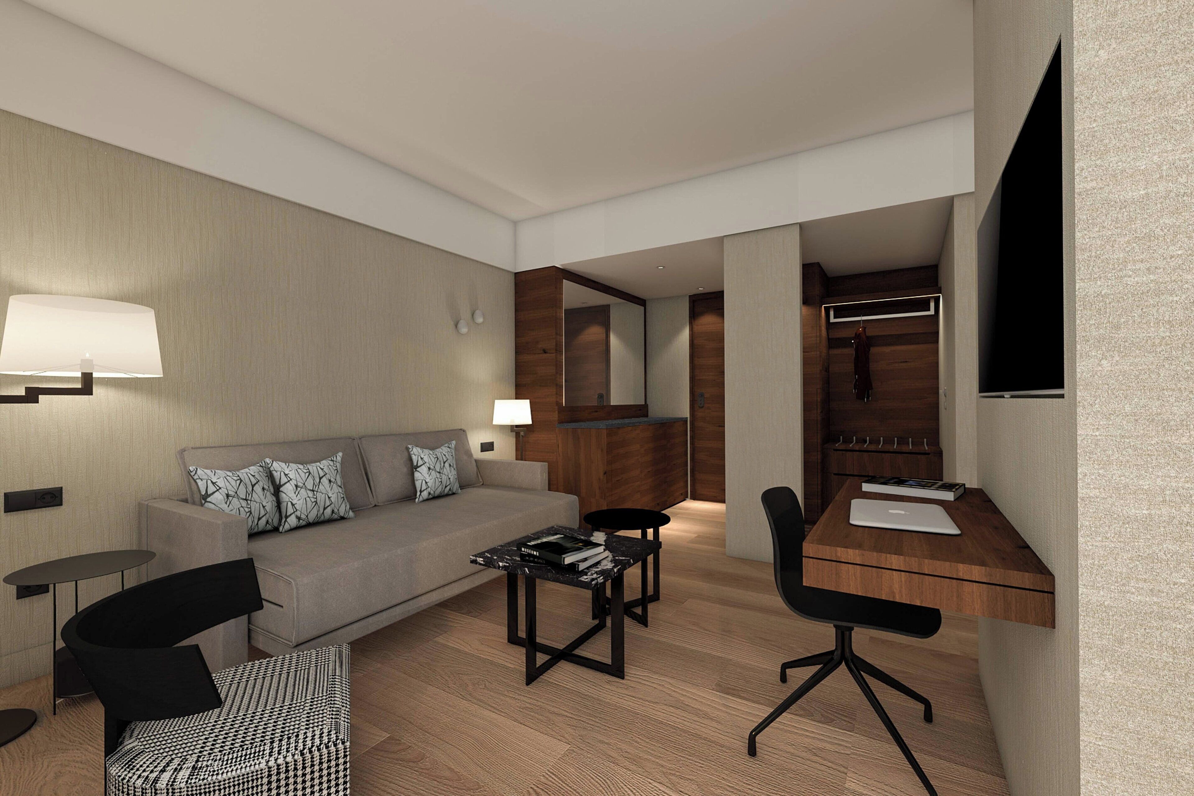 Habitació d'hotel moderna amb un sofà, un escriptori, una cadira, una taula petita i una perxa per abrigos.