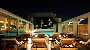 Área de piscina en la azotea con sillones y vista a un jardín iluminado.