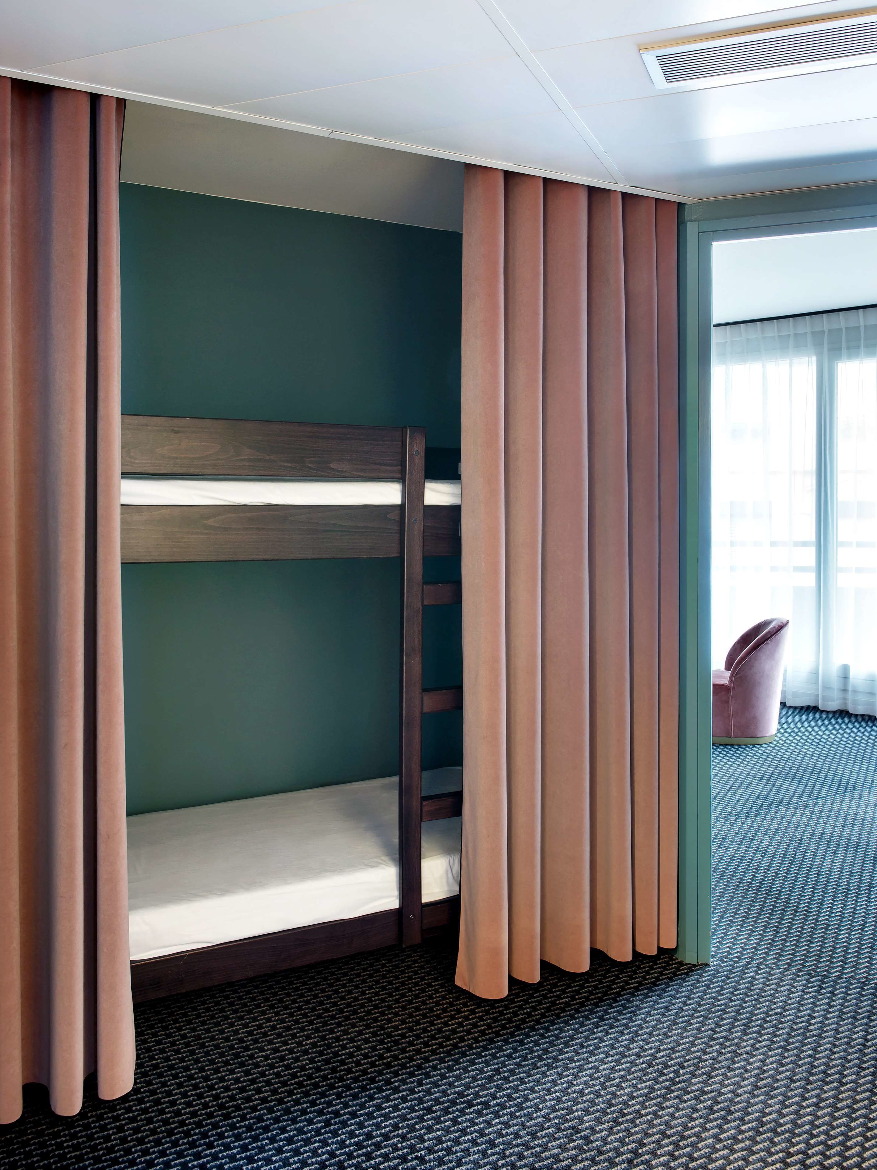 A bunk bed room with a window, curtains, and a chair.