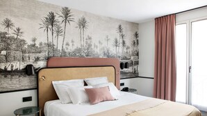 Quarto de hotel com cama, mesa de cabeceira, painel decorativo na parede e janela com cortinas.