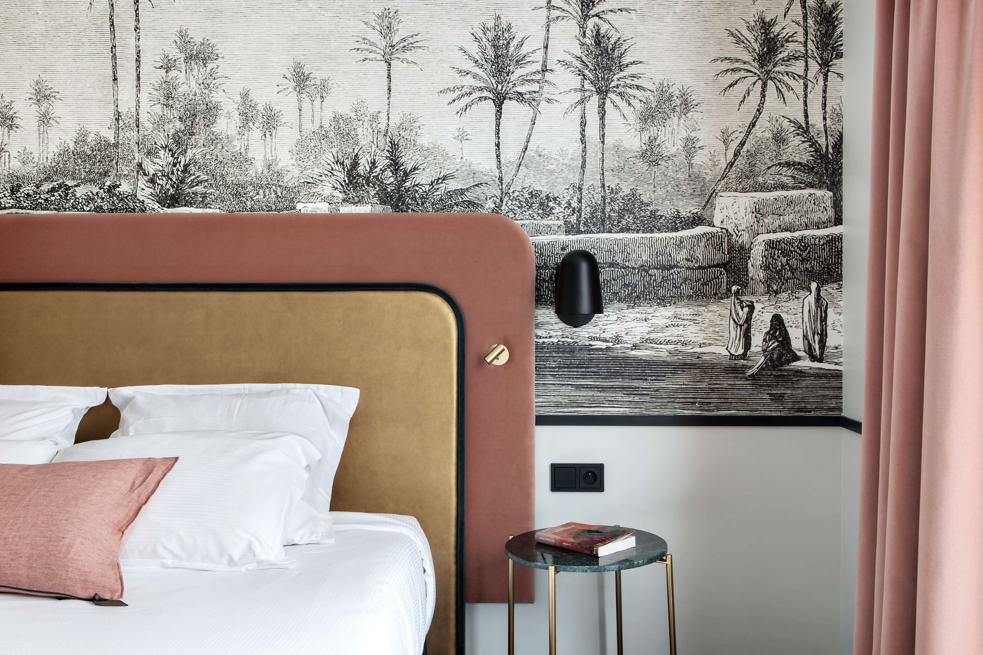 A hotel room with a bed, a small table, and a wall mural depicting a tropical scene.