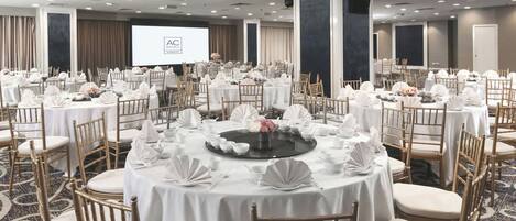 Un salón de conferencias con mesas redondas, manteles blancos y sillas doradas.