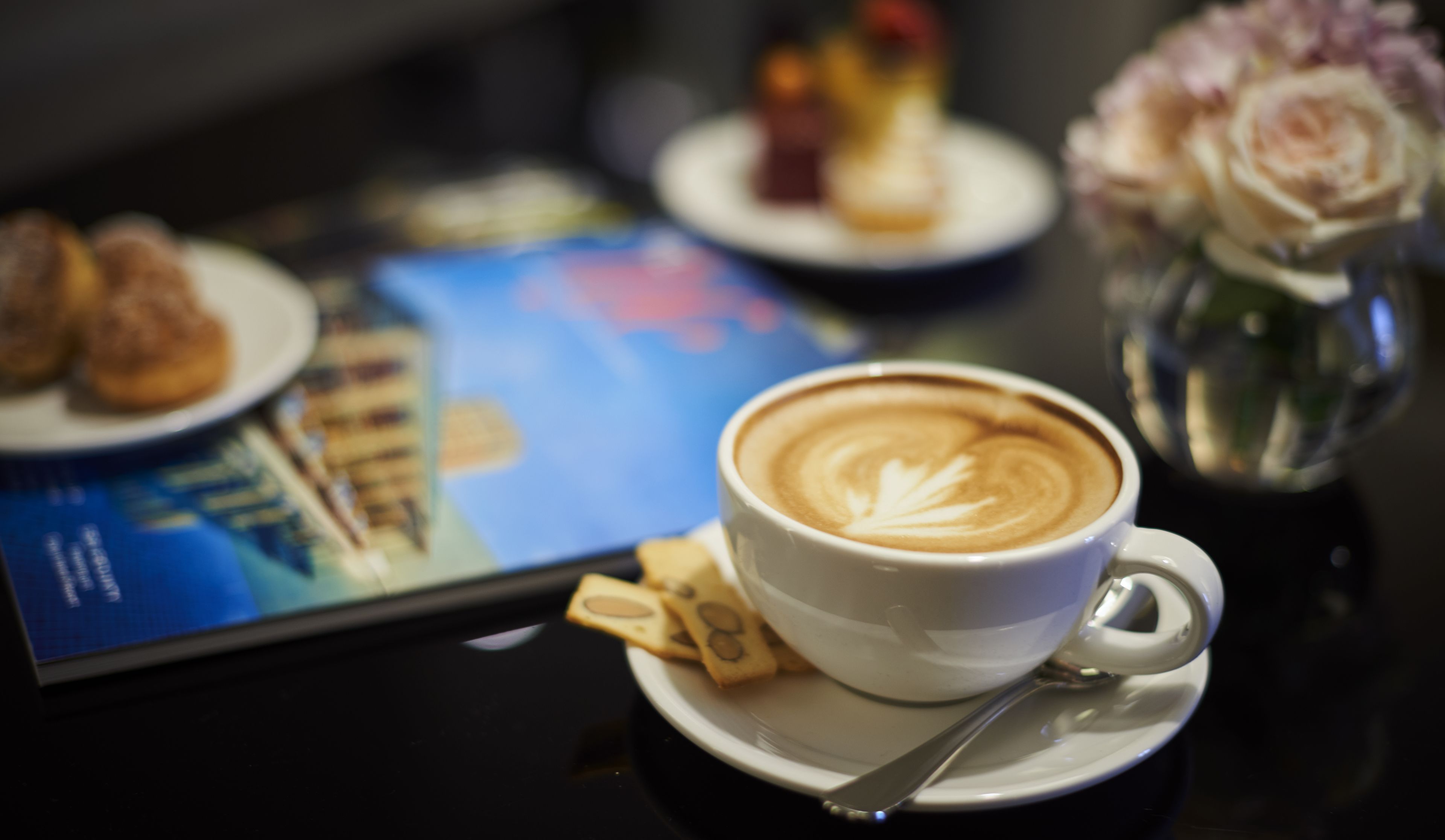 Een kop koffie met latte-art op een schotel, een lepel en een bord met koekjes.