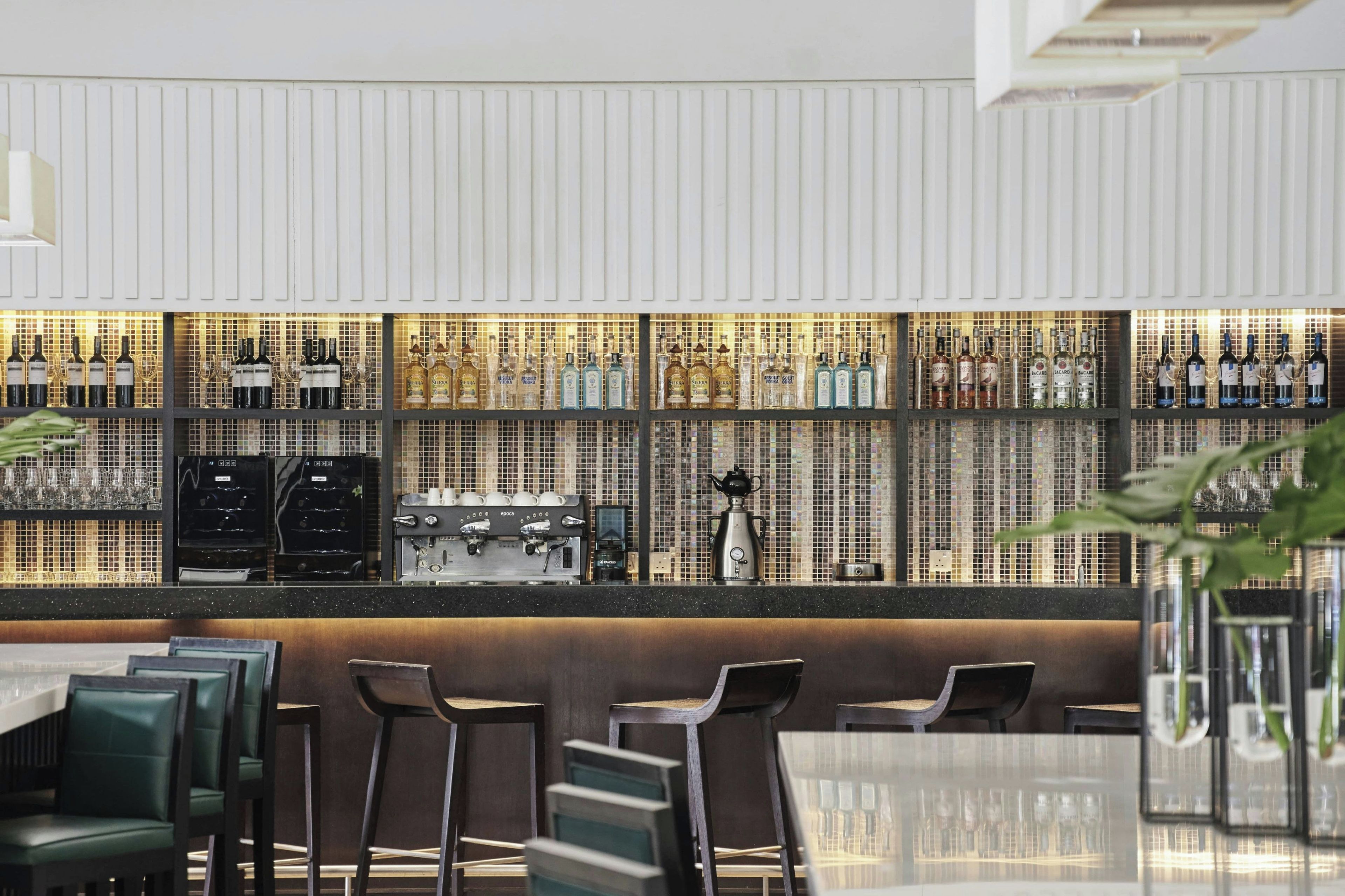 A bar area with multiple shelves of liquor bottles, a coffee machine, and bar stools.