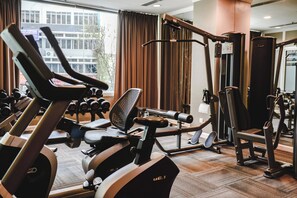 Une salle de sport équipée de matériel d’exercice, notamment des tapis de course et des appareils de musculation, et dotée de grandes fenêtres avec des rideaux.