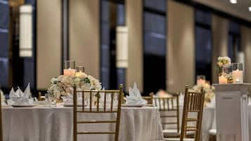 A banquet hall with round tables covered in white tablecloths, gold chairs, and floral centerpieces.