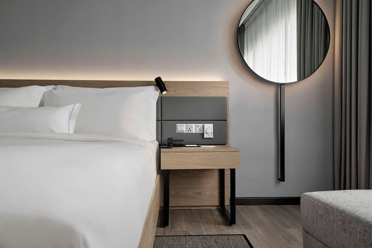 Een moderne hotelkamer met een net opgemaakt bed, een nachtkastje met een lamp, een stopcontact en een spiegel aan de muur.