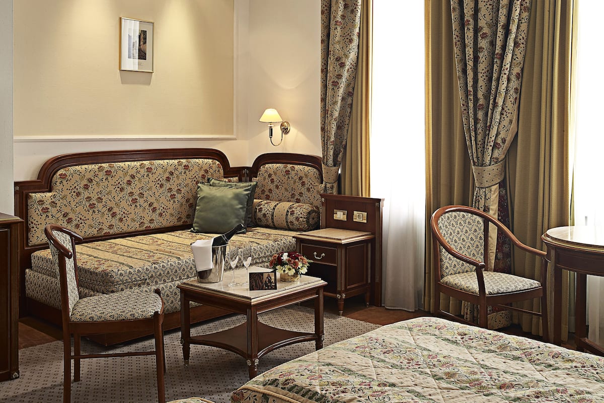 A hotel room with a sofa set, a wooden coffee table, a side table, a chair, and a bed.