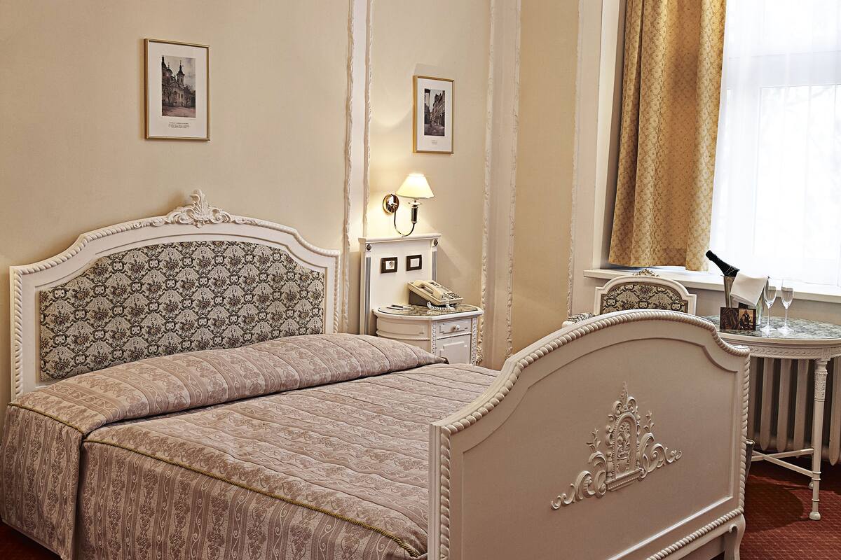 A classic bedroom with a large bed, a bedside table with a lamp, and a small table with a bottle and glasses.