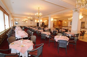 Une salle à manger élégante, dotée de plusieurs tables, de chaises et de lustres.