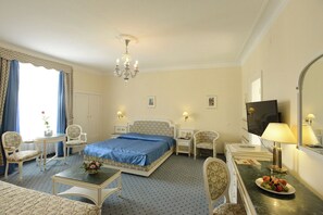 Une chambre d’hôtel avec un lit, deux chaises, une petite table, un bureau, une télévision et une lampe.