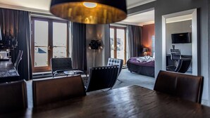A modern hotel room with a dining area, a sofa, a TV, and a large window with curtains. - Scandic Front (Copenhagen)