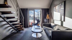 A modern living room with a staircase, a black leather sofa, a round table, and a city view through a glass door. - Scandic Front (Copenhagen)