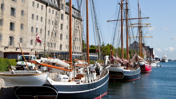 A row of tall ships docked at a harbor with a historic building in the background. - Scandic Front (Copenhagen)