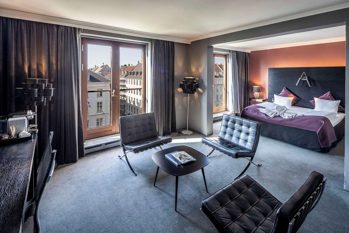 A modern hotel room with a large bed, two armchairs, a small table, and a floor lamp.